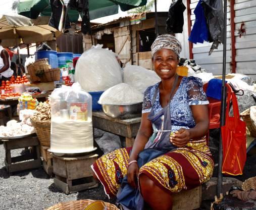 A young vendor carrying a tray of smoked fish through an Accra market