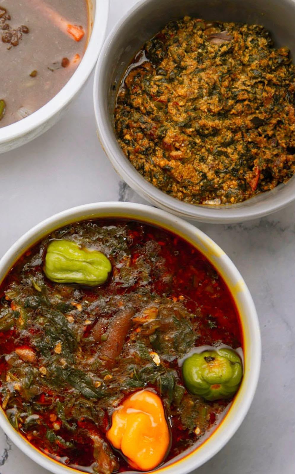 Bowls of palm nut soup and egusi stew garnished with scotch bonnet peppers