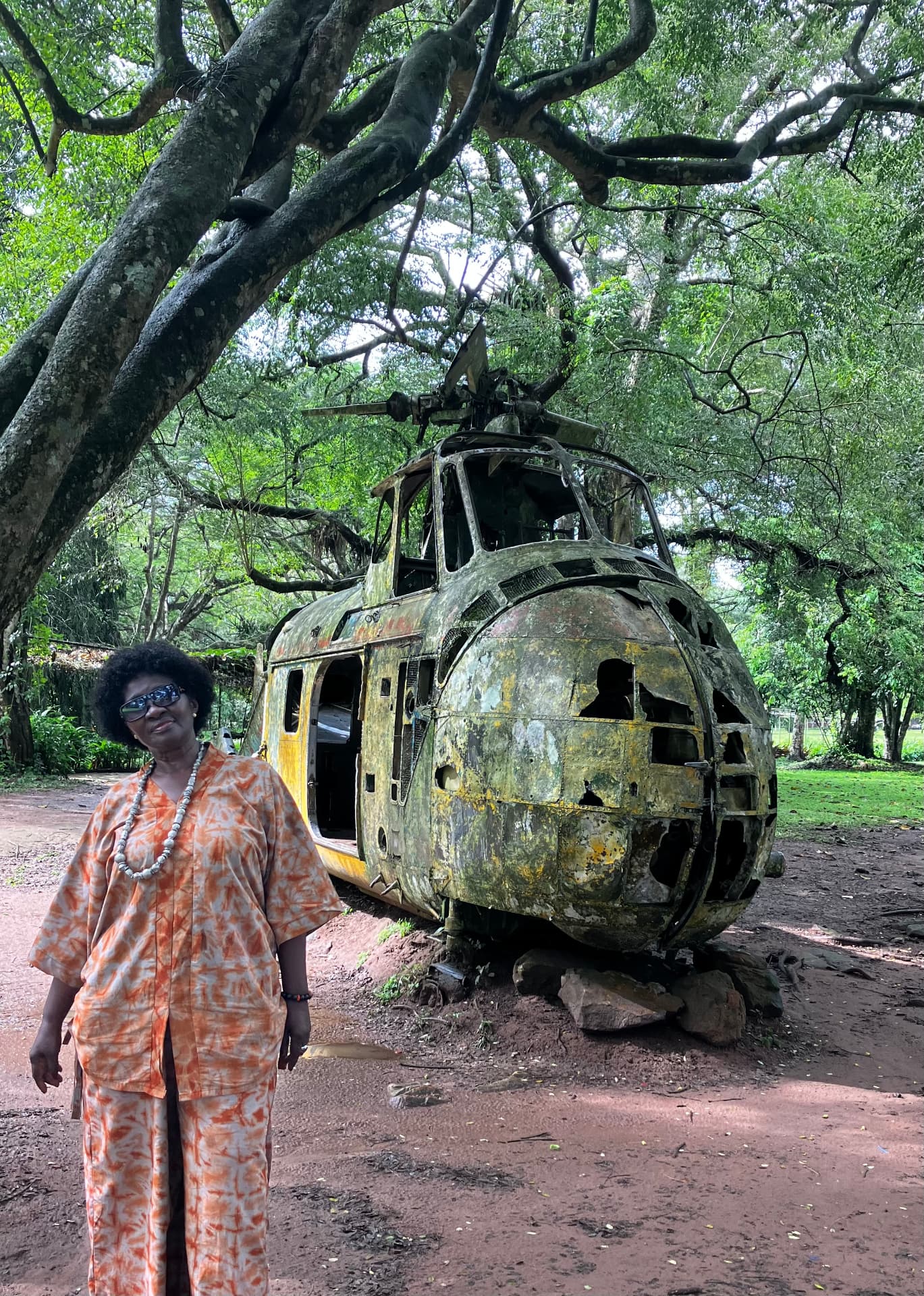A visitor beside a weathered vintage helicopter on the Aburi Gardens & Mampong Cocoa Farm day trip