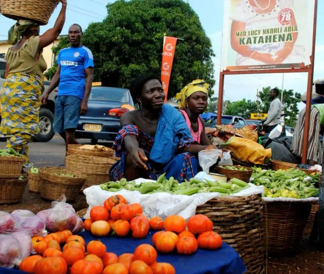 Vendors with baskets of fresh tomatoes and okra at a Ghana market stall