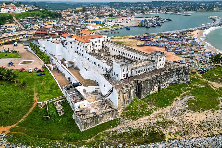 Aerial view of Elmina Castle on its peninsula, ringed by fishing canoes