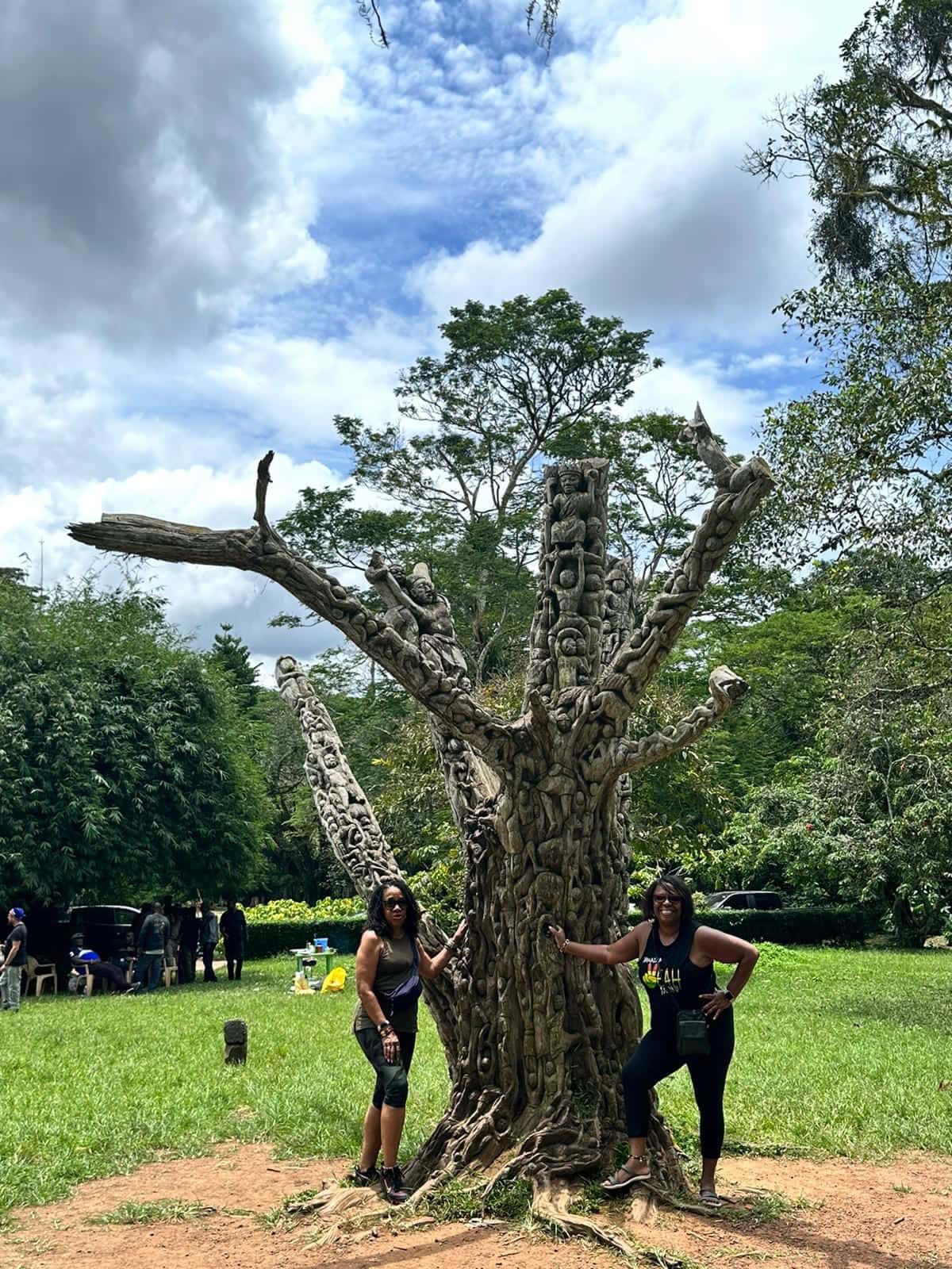 Visitors beside a carved wooden tree sculpture at Aburi Botanical Gardens
