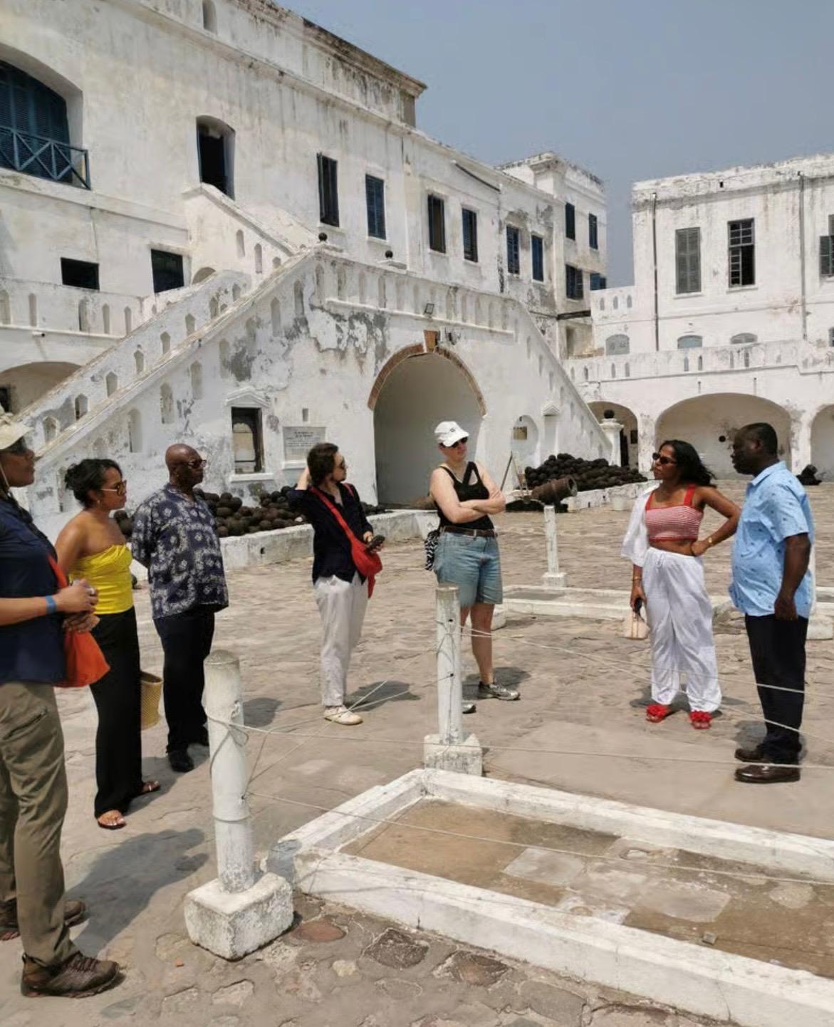 A guided group gathered at a grave marker inside a historic coastal fort